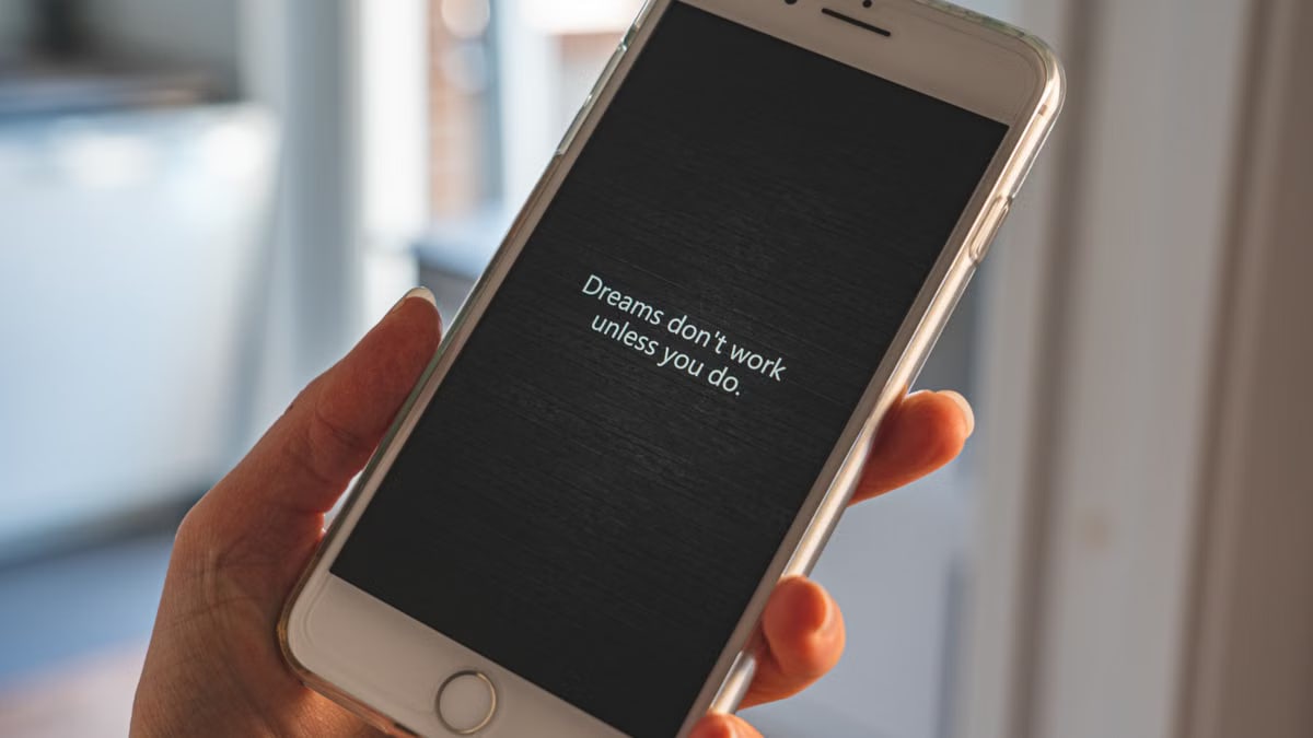 Hand holding smartphone displaying motivational quote: 'Dreams don't work unless you do.'